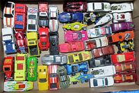 Top-view photo showing 43 diverse Hot Wheels toy cars in a cardboard box with varied colors and designs including flames, stripes, and national flags.