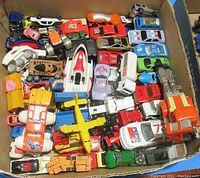 Overhead view of a box filled with assorted diecast toy vehicles showing a mix of cars, trucks, and planes in various colors and conditions.