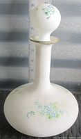 Full view of the white Bristol glass vanity bottle with floral hand painted decoration and stopper, approximately 9 inches tall