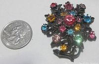 Top-down view of colorful Coro floral branch pin with pink, blue, yellow, and green stones next to a quarter for size comparison.