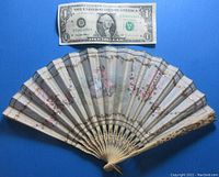 Full view of the small bone fan with Victorian couple painted on the webbing and dollar bill for size reference.