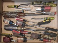 Overview of hand tools including nut drivers, screwdrivers, awls, and hooks piled together showing used condition.