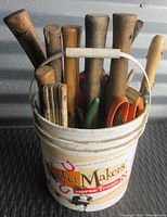 Plastic bucket filled with handles of various hand tools including hammers and snips.