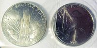 Both coins shown together in original plastic protective sleeves, one with Shuttle Discovery launch design and the other with moon landing anniversary design