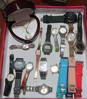 Photo showing a collection of 14 wristwatches of varying styles and materials along with a pendant watch in a heart shaped box.