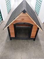 Front view of medium sized wooden dog house with black framed entrance and pitched black tiled roof.