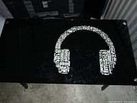 Top view of the black glass table surface showing white headphone graphic made up of musical and sound-related words.
