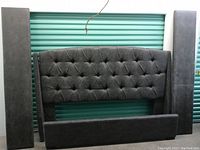Disassembled grey suede king bed frame components including headboard, side posts, footboard panel against storage door