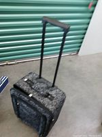 Front angled view showing extendable handle, wheels, and white skull print on black fabric suitcase.