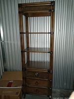 Full view of tall wooden shelf with three open shelves and three bottom drawers with bamboo accent detailing on drawer fronts, sides, and top crown.