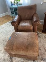 Front view of brown leather-like arm chair with matching ottoman in living room setting.