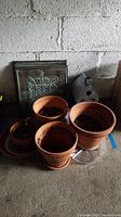 Photo showing four terracotta planters with soil inside, a decorative hanging wall tile with an ornamental pattern, and a metal birdhouse.