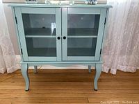 Front view of blue wooden book cabinet with glass doors and curved legs.
