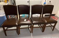 Four matching wooden dining chairs with brown vinyl cushions, showing overall condition and arrangement.
