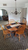 Wooden oval dining table with six matching wooden chairs in room with carpet and hanging chandelier.