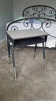 Front view of the metal elementary school desk showing light gray laminate top, black frame, and storage cubby.