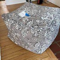 Photo showing the side view of the square foot cushion ottoman covered in grey floral cloth showing its shape and pattern.
