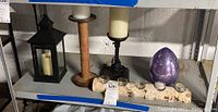 Shelf with multiple candleholders including a tall wooden candlestick, short black candleholder, purple egg-shaped decorative candle, and a metal tea light holder with five small glass tea light holders.