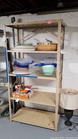 Full view of beige metal shelving unit holding various plastic containers and kitchen items (not included). Unit stands on basement floor.