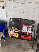Photo of black metal patio bench with perforated design, showing overall structure and front view. Items placed on bench include paint cans, tools, and a Husky contractor bag box.