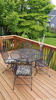 Photo of 5 piece metal mesh patio set on wooden deck, showing round table with umbrella hole and 4 chairs with cushions