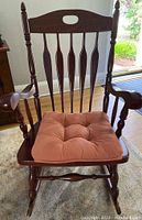 Front view of wooden rocking chair with cushioned seat showing spindle back and armrests.