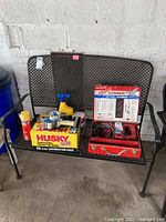 Full view of lot items displayed on a metal bench, including Milwaukee rotary hammer case, Husky contractor bags box, foam sealant, spray applicators, and additional cleaning or repair products.
