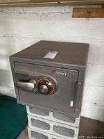 Front view of the gray Sentry Safe showing combination dial lock and handle with some surface dust.