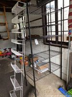 Black wired shelving unit with five open shelves, positioned in garage against wall.