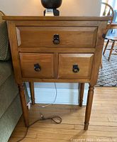 Front view of wooden side table, showing three drawers with metal ring pulls and tapered legs.