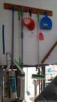 Full view of all cleaning tools hanging on wall including two Swiffer sweepers, rope mop, dust pan, fly swatter, and corner brush.