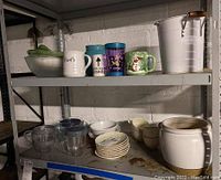 Set of mugs, bowls, a white ceramic pot, and white ice bucket displayed on shelving.