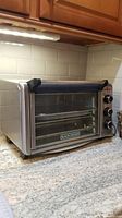 Black & Decker toaster oven on countertop, stainless steel finish, side control knobs visible