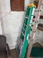 Green and aluminum Werner utility ladder leaning against garage wall with visible use marks and wear.