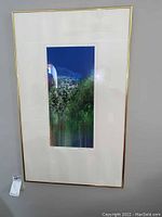 Photo of a large framed art piece with a landscape photograph in blue sky and greenery, with gold frame.
