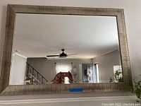 Front view of large rectangular mirror with silver textured frame showing clear reflection and room background.
