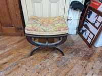 Front view of antique curule stool showing floral upholstered cushion and dark wood base with X-shaped legs.