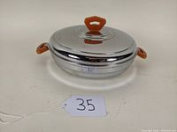Closed view of the warm food plate with lid on, showing the shiny metal warming base with orange-brown Bakelite handles and knob.