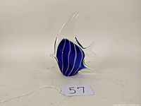Front view of a cobalt blue fish-shaped glass paperweight with clear fins and white accent lines, against a plain background.