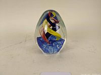 Clear ovoid glass paperweight with colorful internal ribbons shown from front angle on plain background.