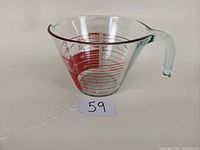 Side view showing the cone shape, pouring spout, clear glass handle, and red measurement markings in cups on the glass measuring cup.