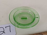 Top view of green uranium glass ashtray showing circular shape with geometric cut pattern on rim and central raised ridge.