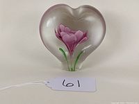 Front view of the heart-shaped glass paperweight with the purple flower inside, showing clear glass and green stems.