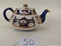 Side front view of Imari style porcelain teapot showing body, handle, and spout with decorative patterns.