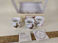 Three Lenox Butterfly Meadow votive holders displayed outside of box with original packaging and information cards.