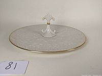 Full view of white porcelain serving plate with embossed patterns and gold trim, central decorative handle.