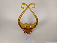 Full view of mid-century amber glass basket with crossed handles on top and clear glass feet at base.