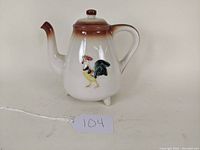 Front view of white pottery coffee pot with brown gradient top and a colorful rooster painted on the side.