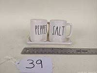 Front view of salt and pepper shakers on tray with ruler for scale.