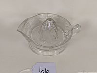 Clear vintage Depression glass citrus reamer with criss cross etched pattern, showing front and side views including spout and handle.